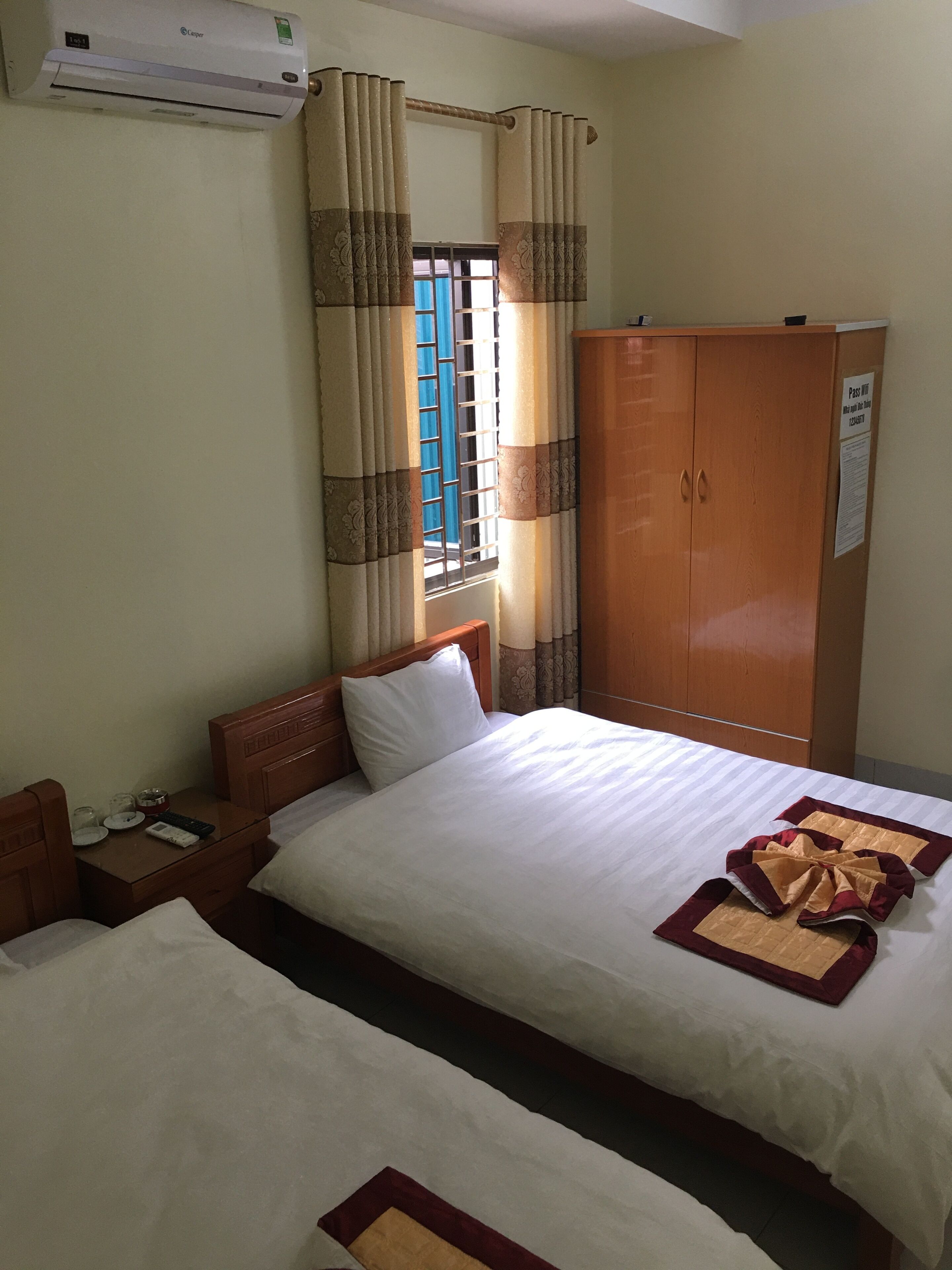 A hotel room with a bed, a wardrobe, a window with curtains, and an air conditioning unit.