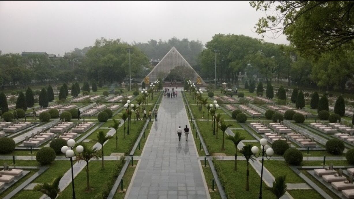 A cemetery with a central pathway, rows of headstones, and a triangular monument.