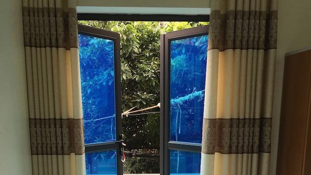 A room with a bed, curtains, and a view of an outdoor area with a railing and greenery. - Duc Thang Guest House (Dien Bien Phu)