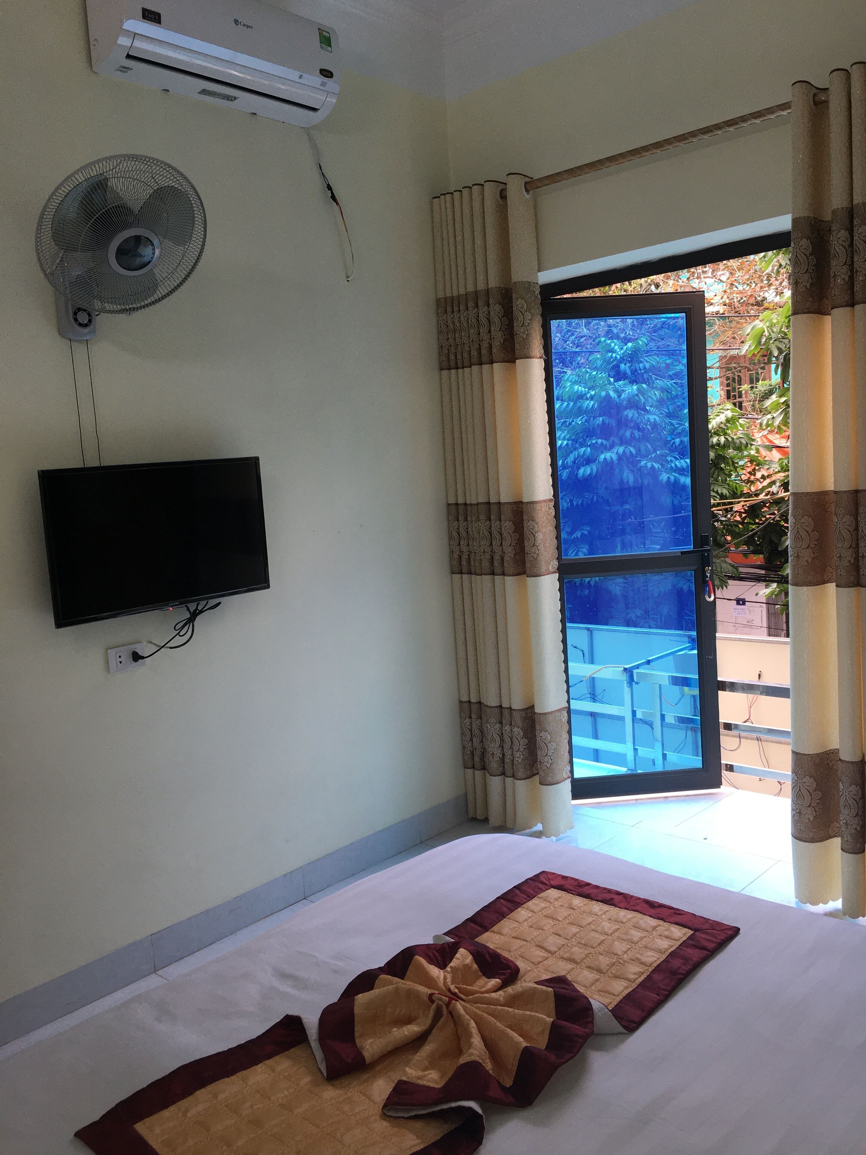A hotel room with a bed, a TV mounted on the wall, an air conditioner, and a window with curtains.