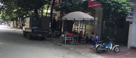 Una calle con un camión estacionado, un pequeño puesto de ventas bajo una tolda y una moto.