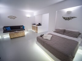 Un dormitorio moderno y minimalista con una cama grande, un sofá, una mesita de centro y una zona de kitchenette.