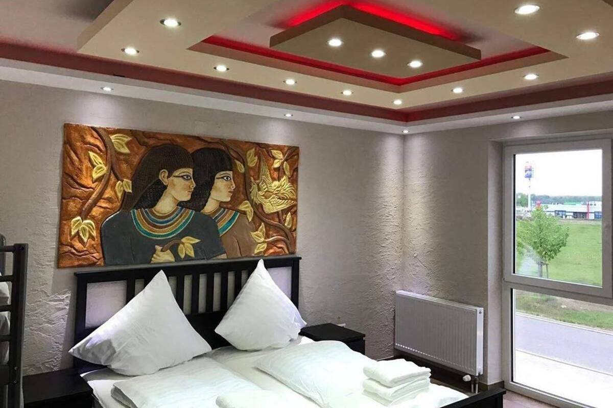 A hotel room with a bed, a nightstand, a painting, and a window with a view of the outside.