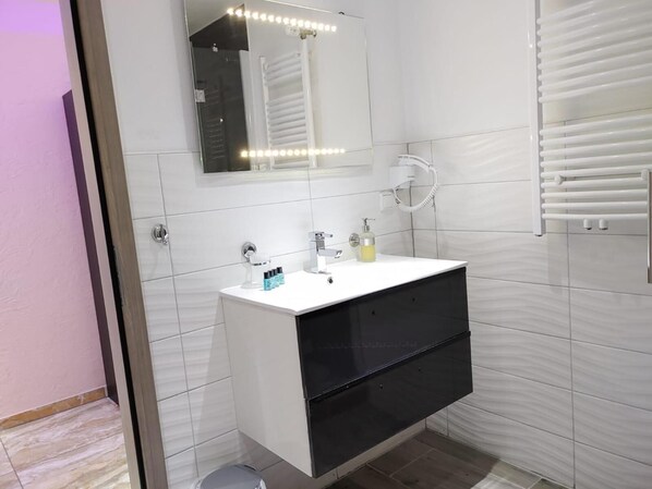 Un baño moderno con tocador blanco, un espejo con iluminación, toallero y zona de ducha.