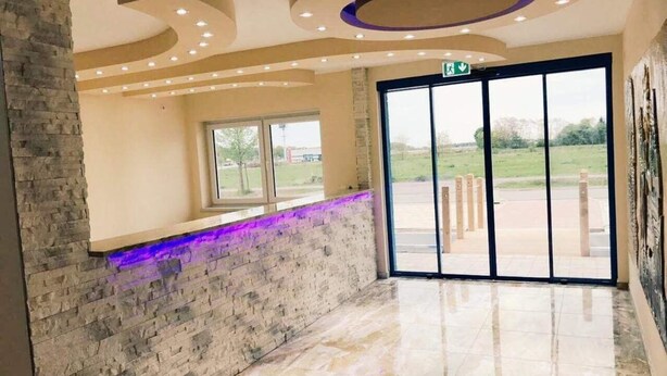 A lobby with a stone wall, a window, and a large glass door leading outside. - Hotel Babylon (Ringsheim)