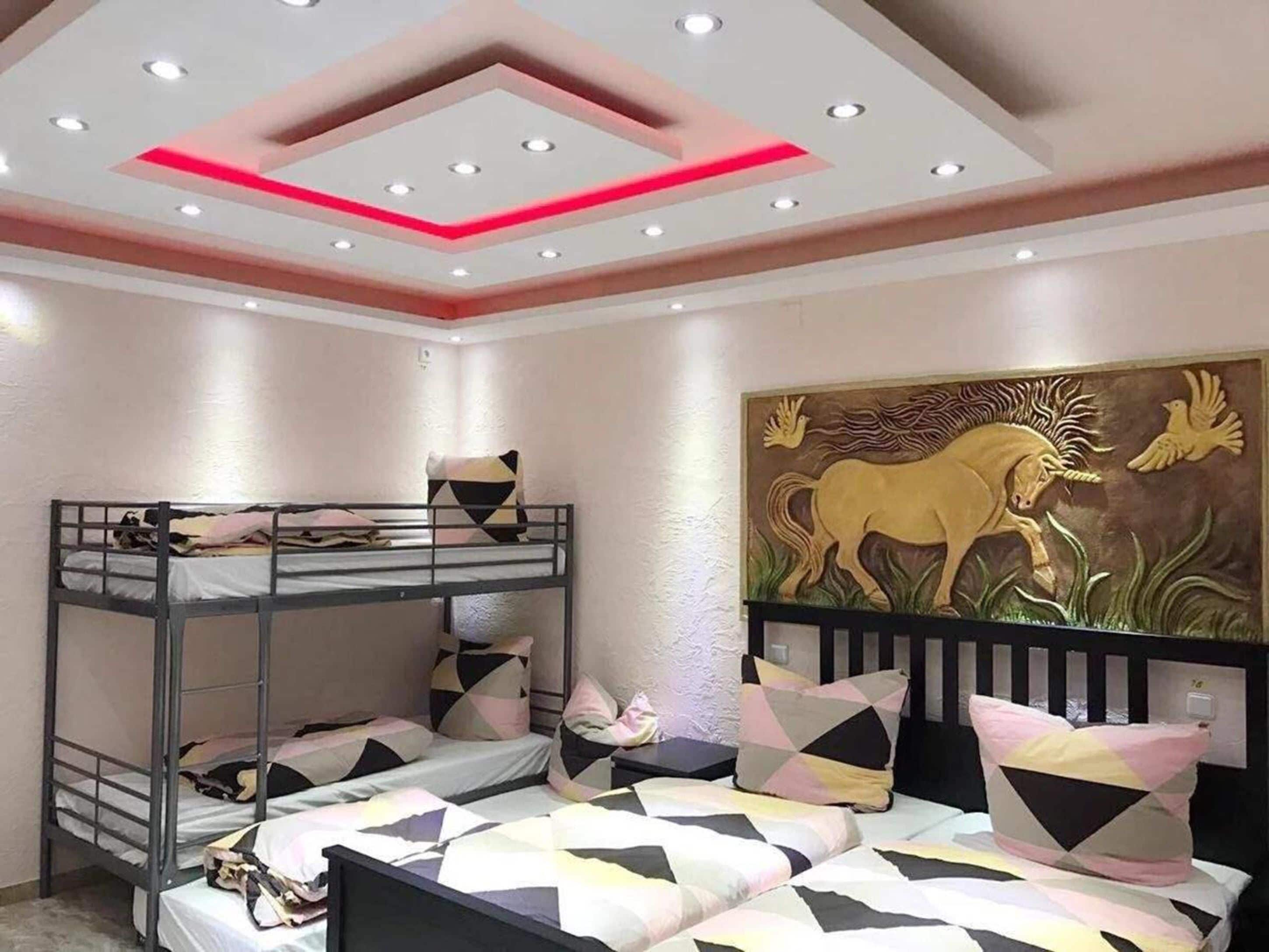 A bunk bed room with a geometric-patterned bedspread, a decorative ceiling with recessed lighting, and a wall mural of a horse and bird.