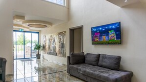 A lobby with a marble floor, a sofa, a wall with a colorful advertisement, and a large window. - Hotel Babylon (Ringsheim)