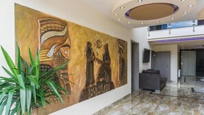A lobby with a large mural, a potted plant, a grey sofa, and a marble floor. - Hotel Babylon (Ringsheim)