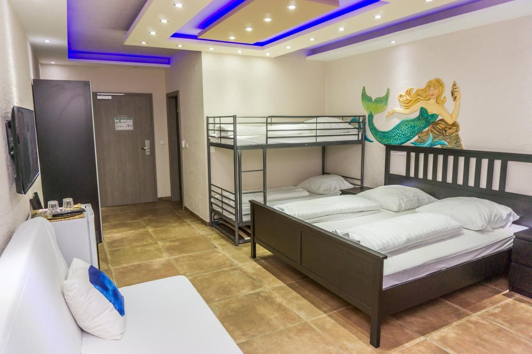 Une chambre d’hôtel avec des lits superposés, un lit simple, une télévision et une fresque murale.