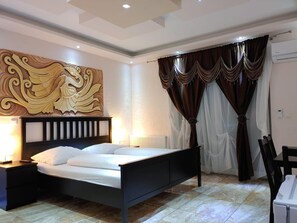 A bedroom with a bed, nightstands, a wall-mounted artwork, curtains, and a radiator. - Hotel Babylon (Ringsheim)