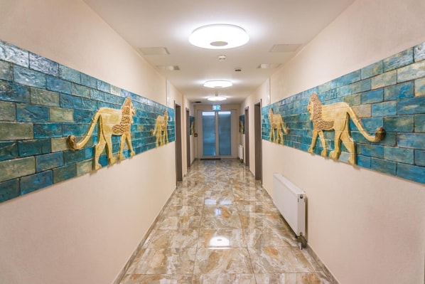 A hallway with tiled walls featuring elephant designs, a marble floor, and a ceiling with recessed lighting. - Hotel Babylon (Ringsheim)