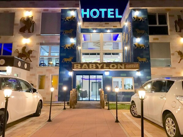 A hotel named 'Babylon Hotel' with a prominent entrance, two parked cars, and decorative lion statues on the facade. - Hotel Babylon (Ringsheim)