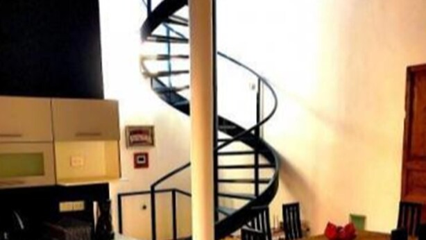 A modern kitchen with a spiral staircase, a dining table with red chairs, and a microwave. - Lofts El Sueño (Puebla)