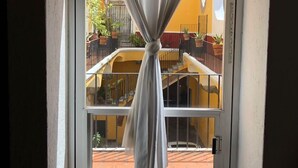 A window with a white curtain tied at the top, overlooking a balcony with potted plants and a yellow building in the background. - Lofts El Sueño (Puebla)