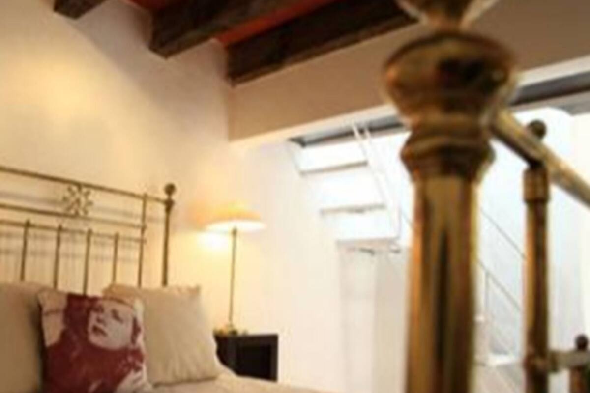 A bedroom with a bed, a nightstand, a lamp, and a window with a view of the outside.