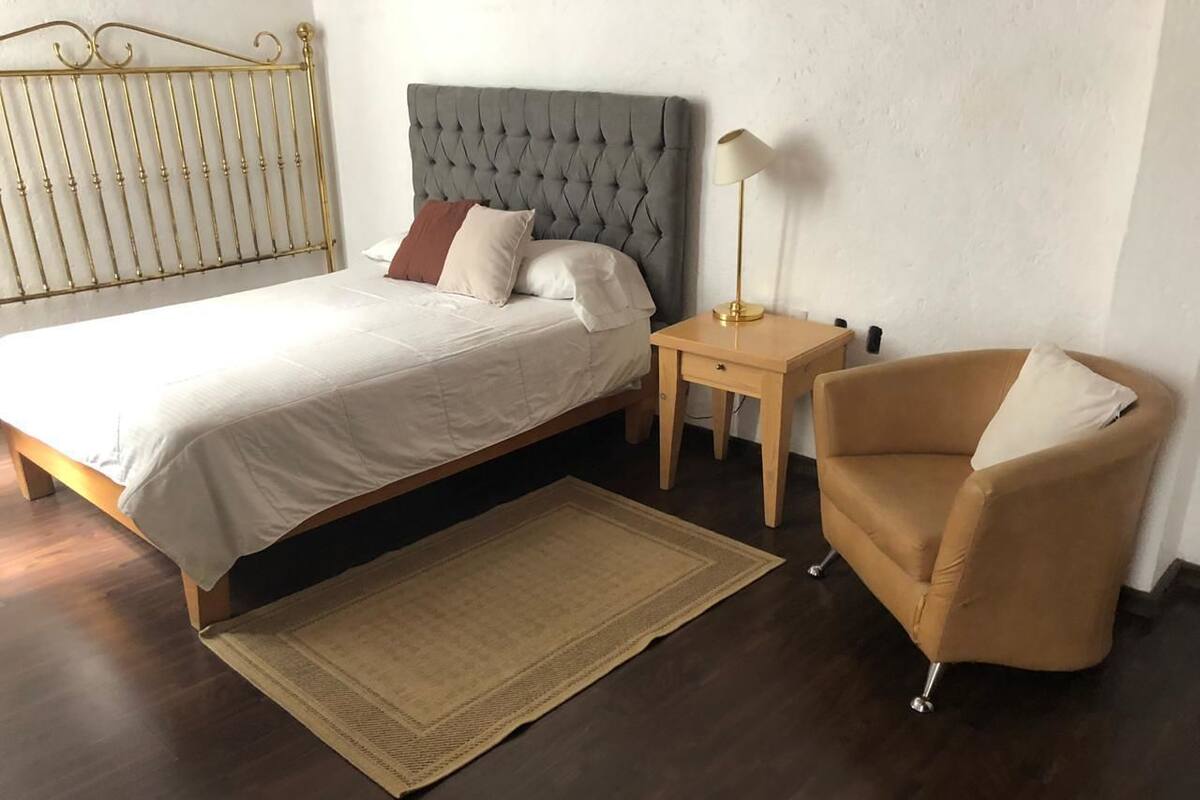 A bedroom with a bed, bedside table, lamp, and a chair.