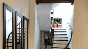 A spiral staircase with black steps and wooden handrails, leading to a landing with a small window and potted plants. - Lofts El Sueño (Puebla)