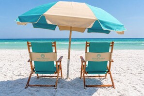 Zwei Strandstühle mit einem Sonnenschirm am Sandstrand.