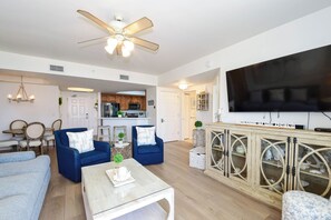 A spacious living area with a ceiling fan, a television, and a kitchen in the background.