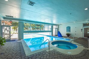An indoor swimming pool with a clear view of the outside, a hot tub, and a poolside area with a covered seating area.