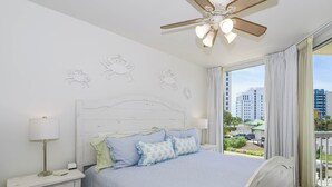 Camera da letto con un letto, comodini, una ventola a soffitto e una finestra con vista sugli edifici.