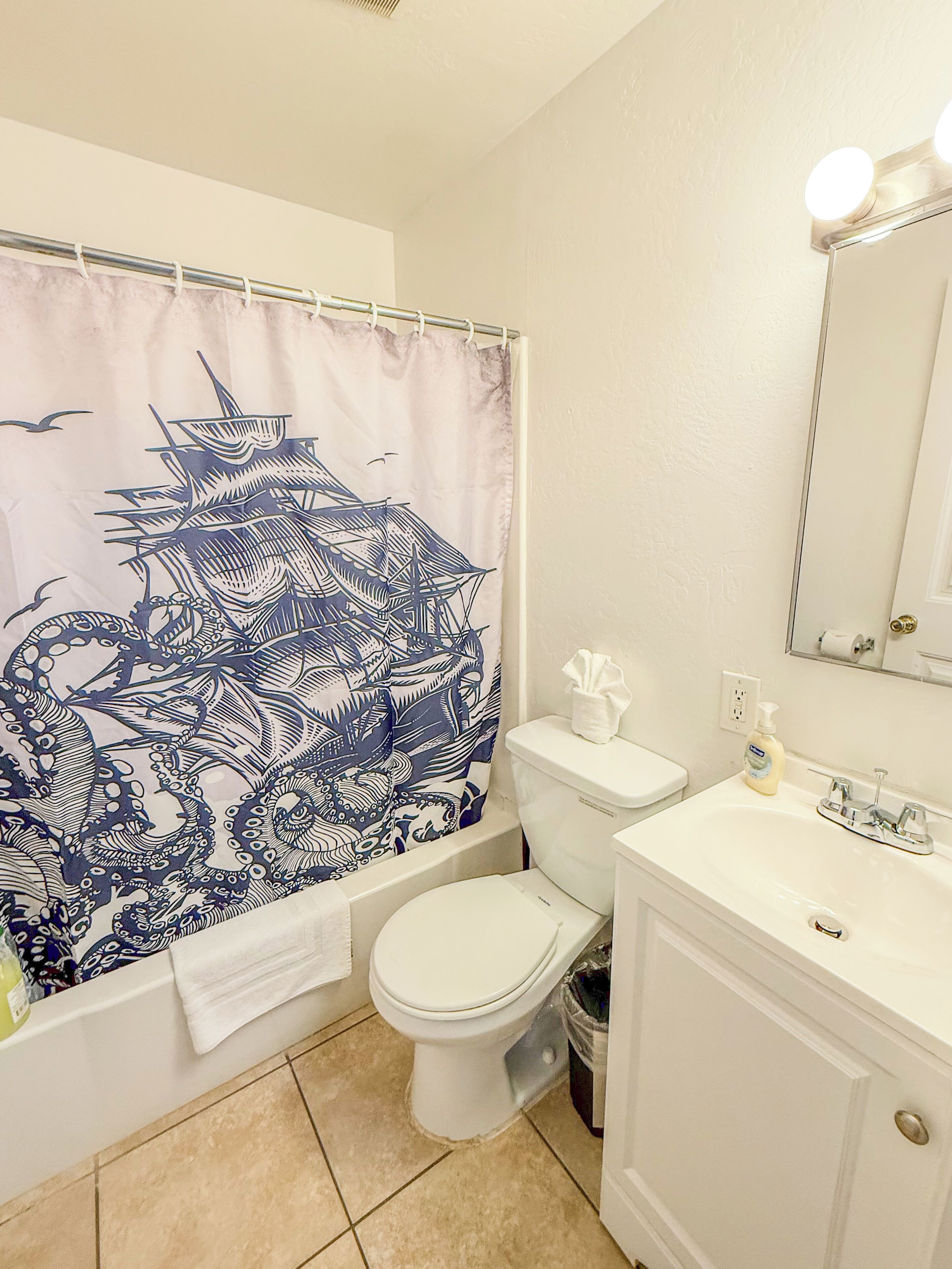 Een badkamer met een wit toilet, een wastafel met spiegel en een douchegordijn met een ontwerp van een blauwe octopus.