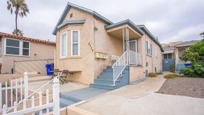 A single-story house with a blue staircase, a white picket fence, and a small patio area.