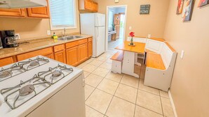 A compact kitchen with a gas stove, sink, and wooden cabinets. A small dining area with a bench and table is adjacent to the kitchen.