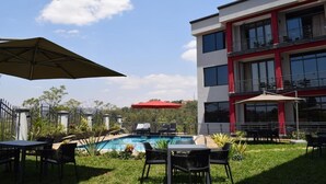 A modern building with a swimming pool, outdoor seating, and a red umbrella. - Mythos Boutique Hotel (Kigali)