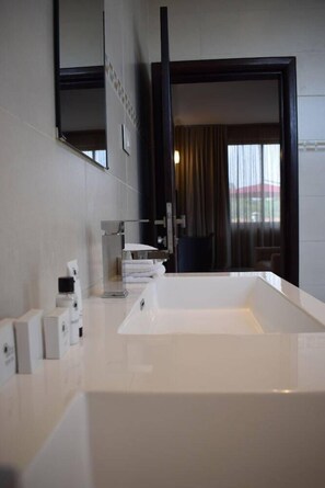 A modern bathroom with a large white sink, a mirror, and a view of the outside through a window. - Mythos Boutique Hotel (Kigali)