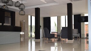A modern lobby with a reception desk, seating area, and large windows offering a view of greenery. - Mythos Boutique Hotel (Kigali)