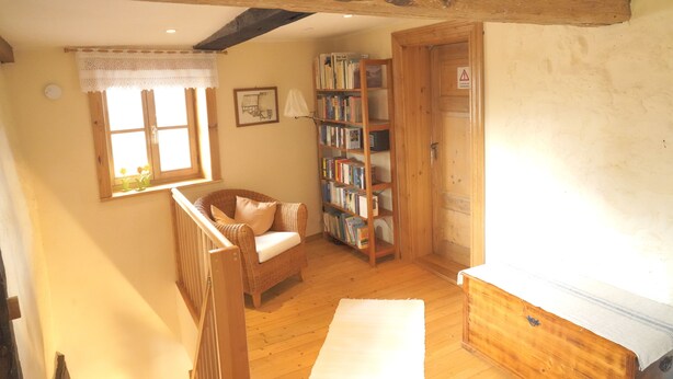 A cozy room with a wooden ceiling, a bookshelf, a wicker chair, and a radiator. - Ferienhaus am Solling (Dassel)