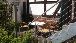 A traditional half-timbered house with a white and brown exterior, a wooden staircase, and a small outdoor seating area with wicker chairs and a table. - Ferienhaus am Solling (Dassel)