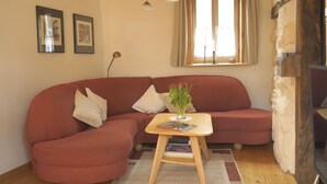 A living room with a red sofa, a small wooden table with a vase of flowers, and a window with curtains. - Ferienhaus am Solling (Dassel)