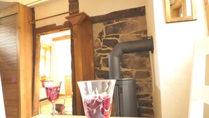 A rustic interior with a stone wall, a wood-burning stove, and a table with a glass of red wine. - Ferienhaus am Solling (Dassel)