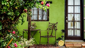 A rustic wooden chair and table set against a green wall, with a window and door visible. - Posada San Antonio (Valle de Guadalupe)