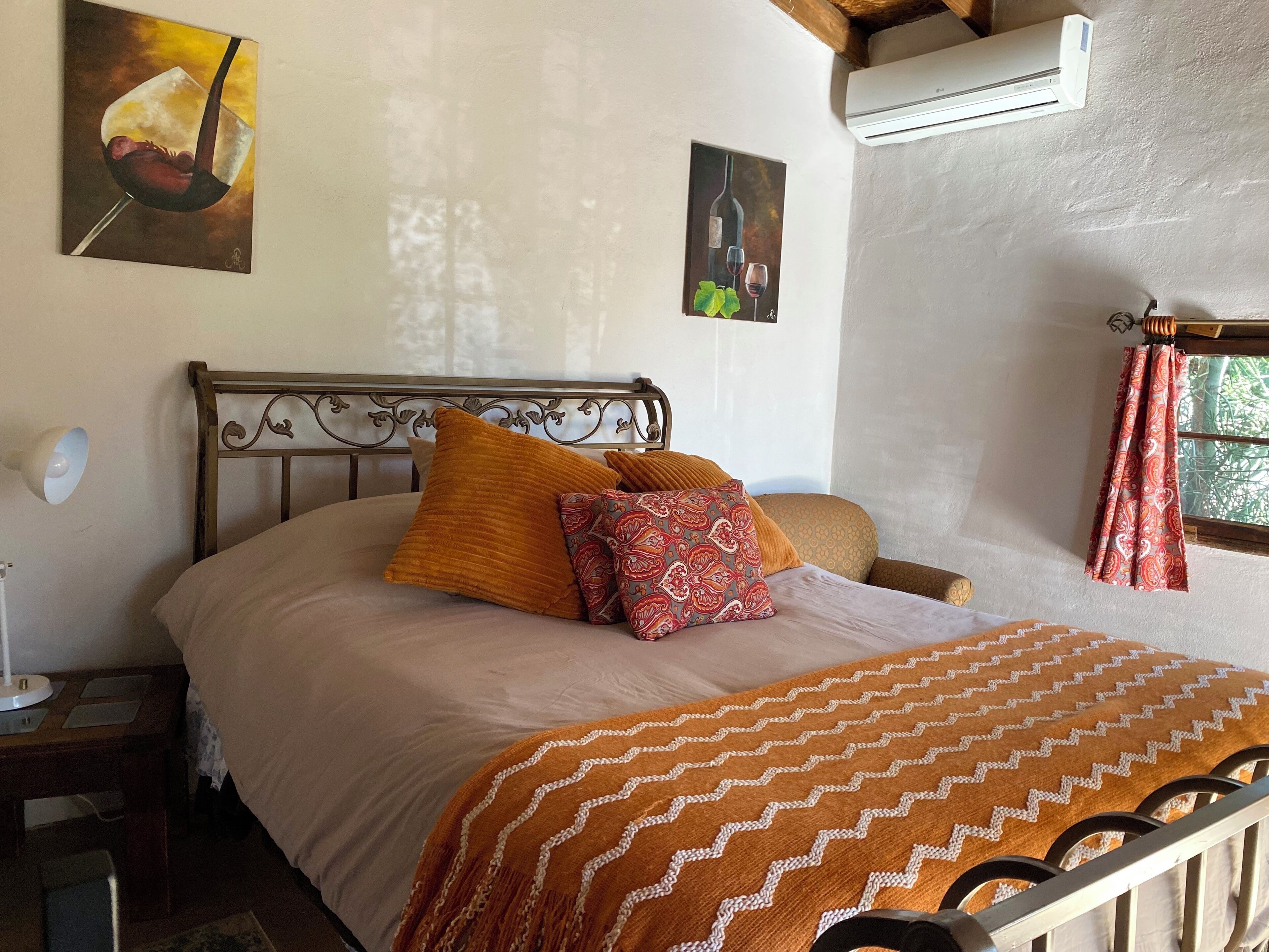 Cama bem arrumada com manta estampada, luminária de cabeceira e duas obras de arte na parede retratando comida e vinho.