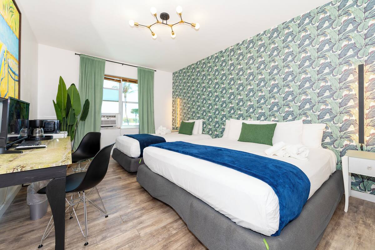 A modern hotel room with a large bed, a desk with a computer, and a green plant.