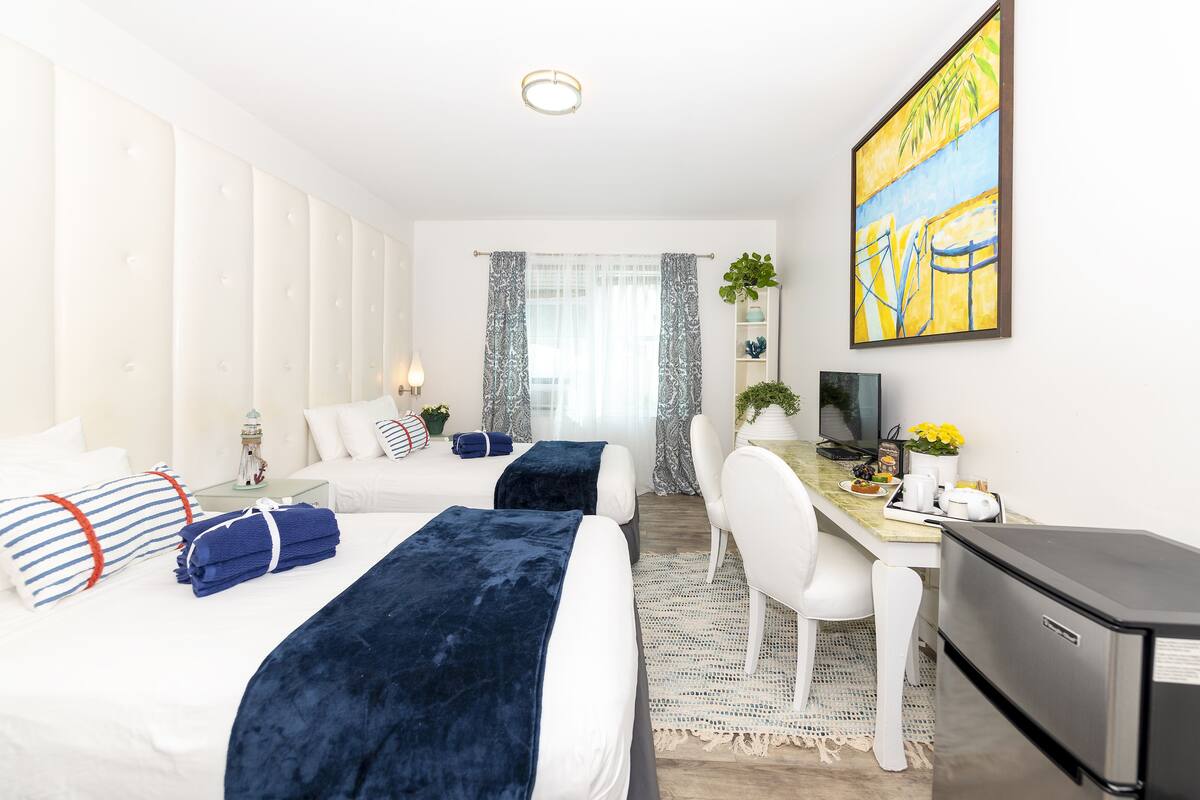 A hotel room with two beds, a desk, a TV, and a refrigerator.