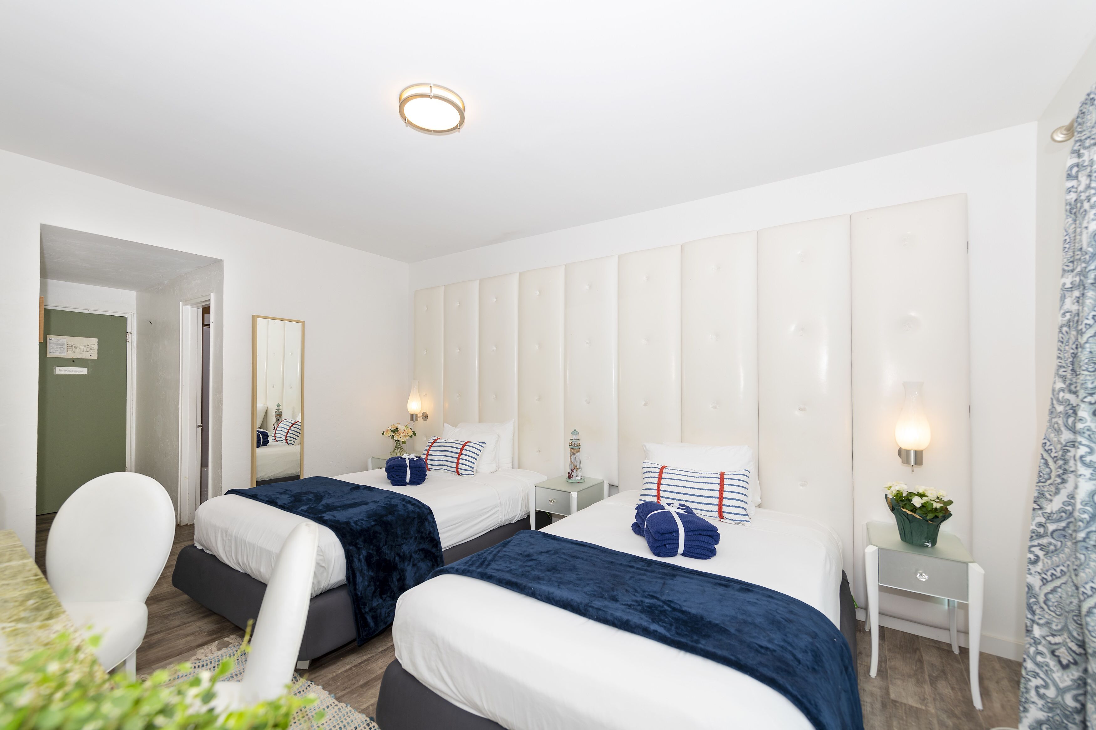 A hotel room with two beds, a small table, a chair, and a mirror.