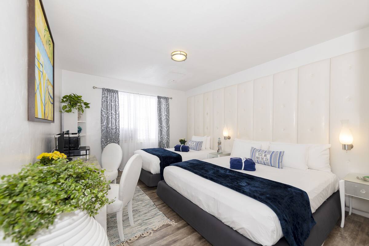 A modern hotel room with two beds, a desk, and a chair.