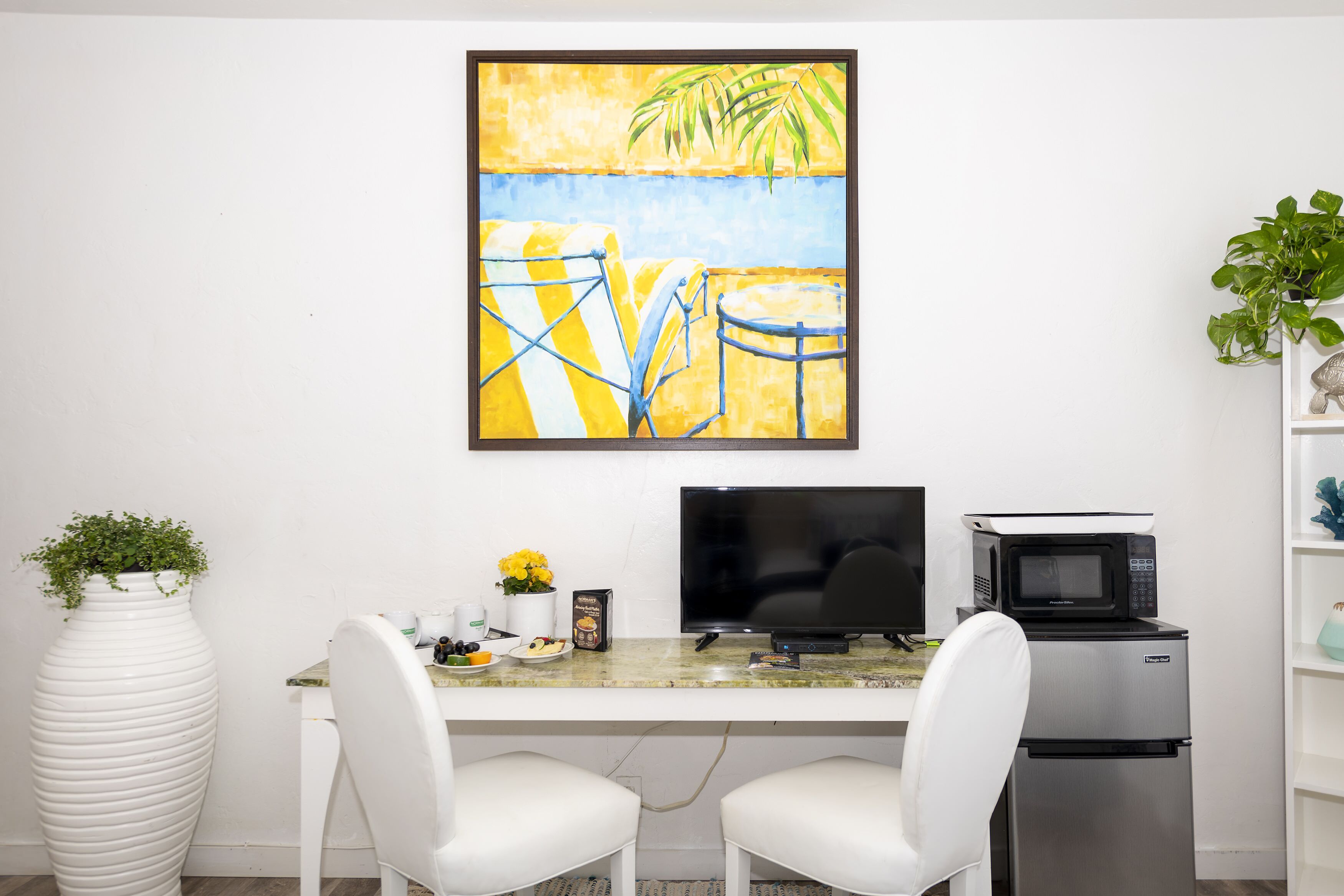 A modern kitchen with a white countertop, two white chairs, a black TV, a microwave, and a refrigerator.