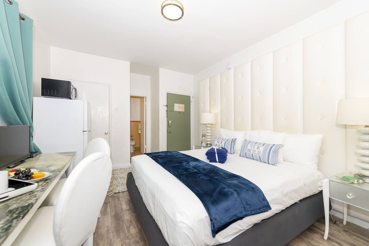 A modern bedroom with a bed, bedside table, and a desk with a computer and breakfast items.