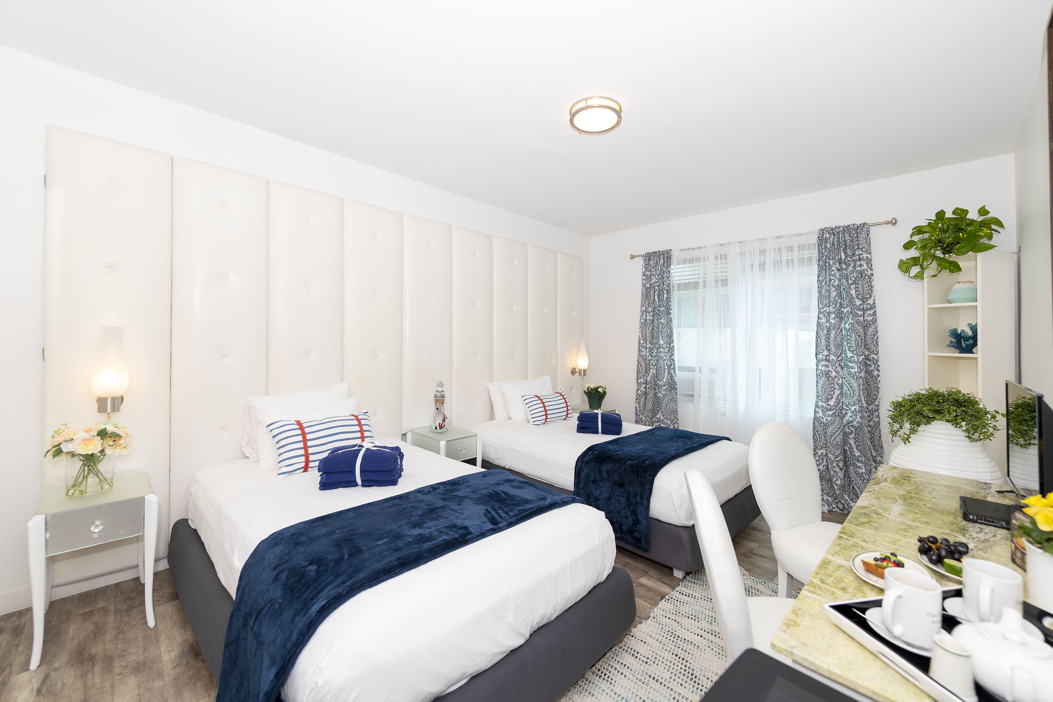 A modern hotel room with two beds, a dining table, and a small seating area.