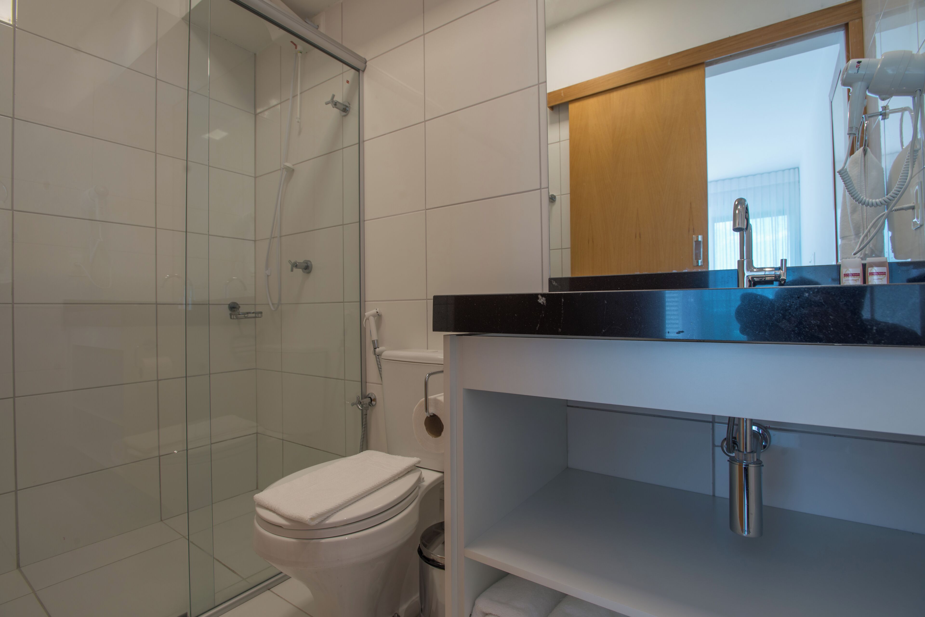 Um banheiro moderno com box de vidro, vaso sanitário branco e toucador com espelho.
