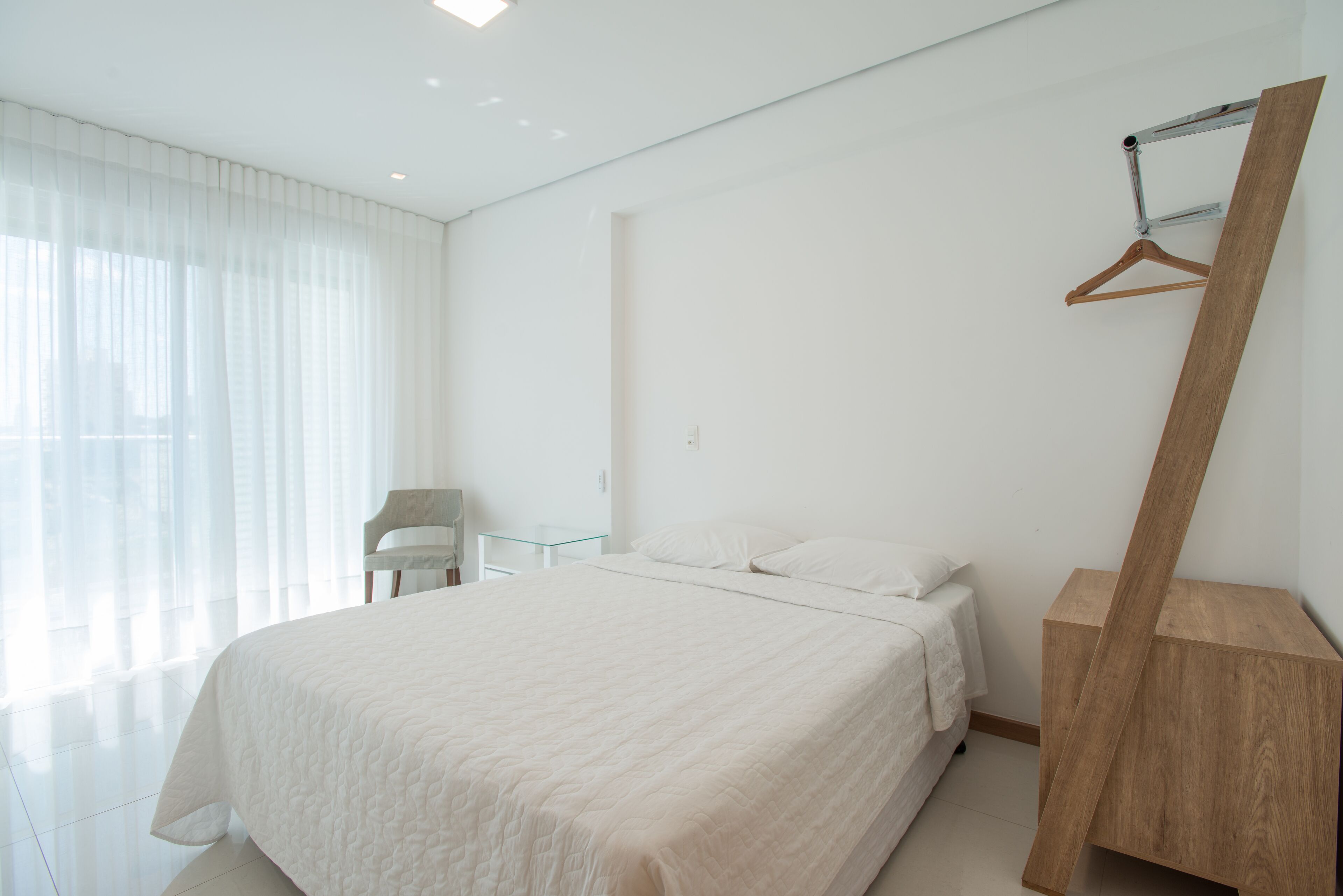 Ein modernes Schlafzimmer mit einem großen Bett, einem Holztischchen, einem Sessel und einem Kleiderhaken.