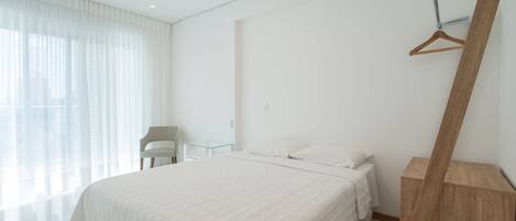 Ein modernes Schlafzimmer mit einem großen Bett, einem Holztischchen, einem Sessel und einem Kleiderhaken.
