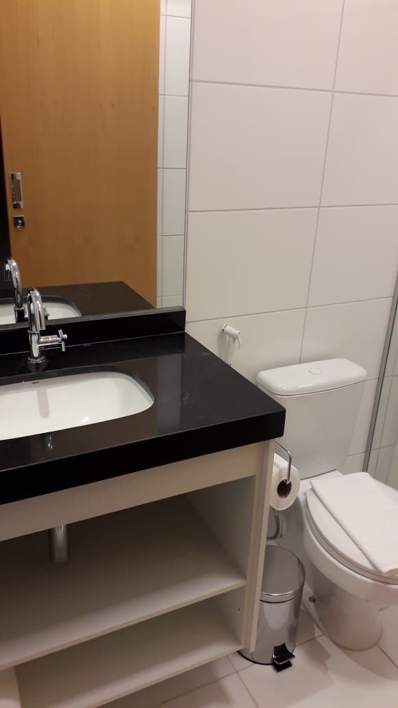 A bathroom with a black countertop sink, a mirror, a white toilet, and a trash bin.