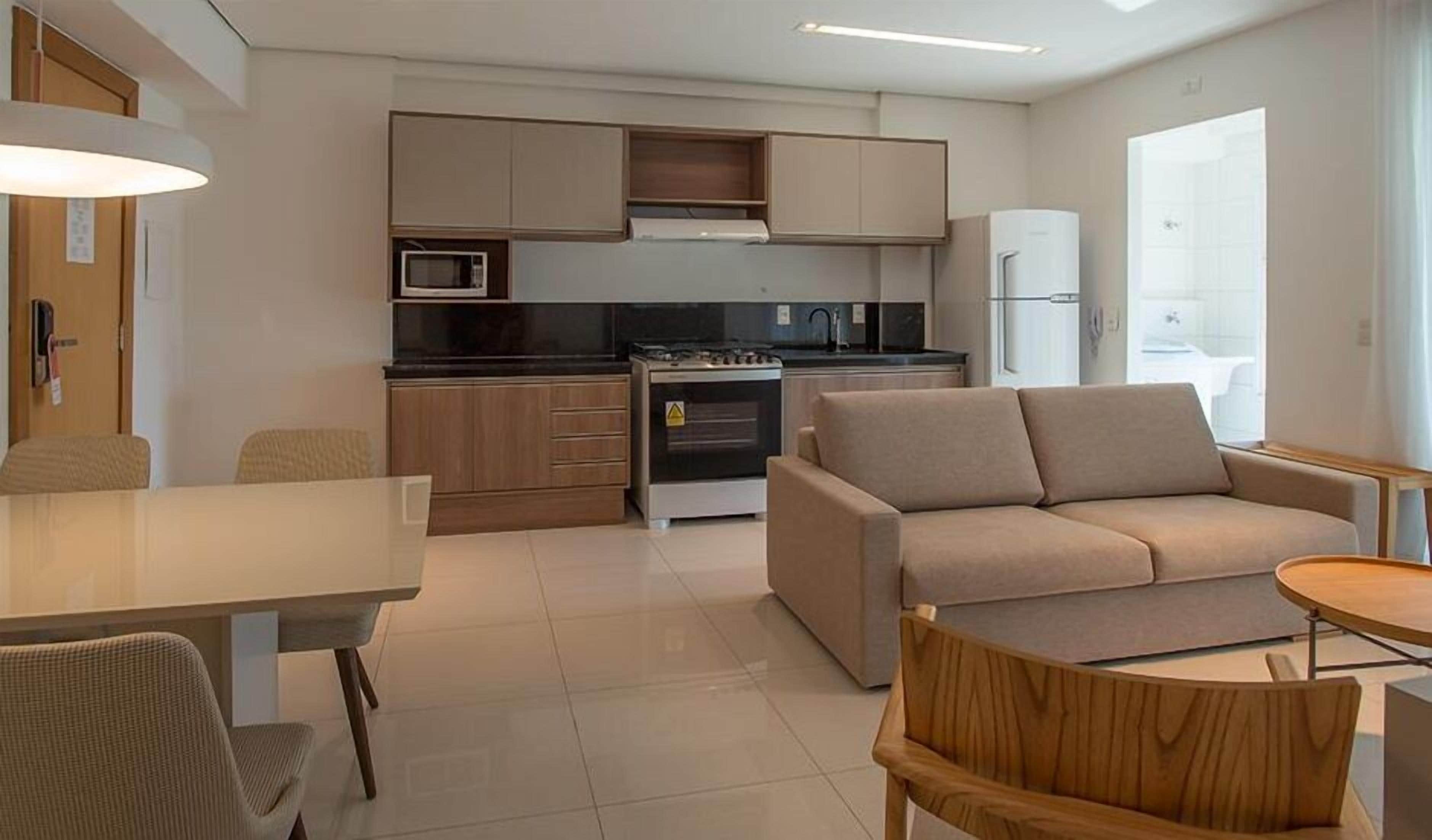 A modern kitchen with a stove, microwave, and refrigerator. There is a dining area with a table and chairs, and a sofa in the living area.