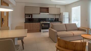 A modern kitchen with a stove, microwave, and refrigerator. There is a dining area with a table and chairs, and a sofa in the living area.